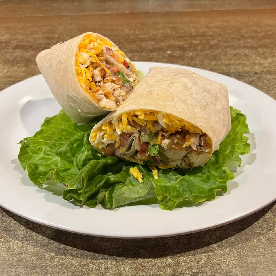A sliced Rebel SmokeHouse burrito, filled with meat, cheese, and vegetables, on a bed of lettuce.