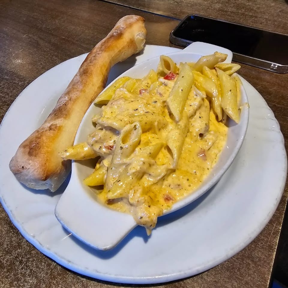 Creamy mac and cheese with penne pasta and a side of bread on a white plate.
