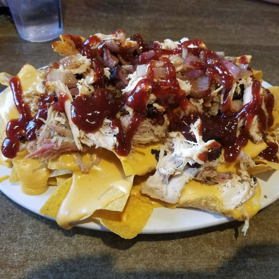 A plate of Rebel SmokeHouse nachos with pulled pork, cheese, red onions, and barbecue sauce.