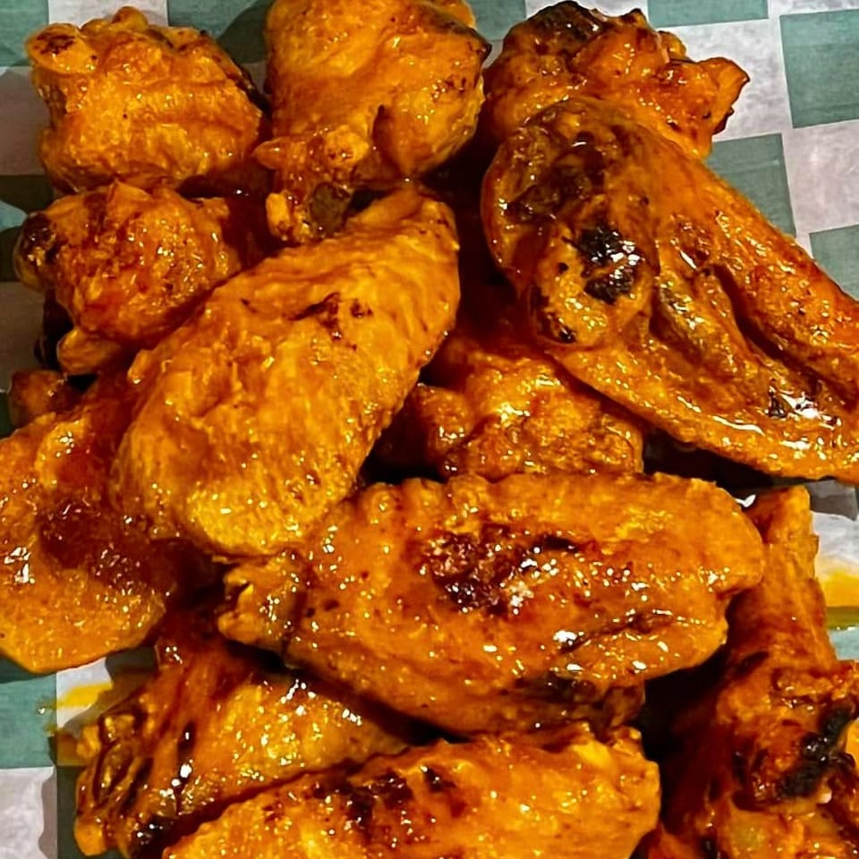 Close-up of Rebel SmokeHouse and Burgers' BBQ chicken wings, glistening with sauce on checkered paper.