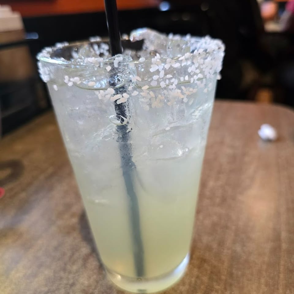 A Rebel SmokeHouse margarita with a salted rim and black straw, filled with ice.